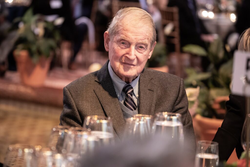 an older man sitting at a table with wine glasses